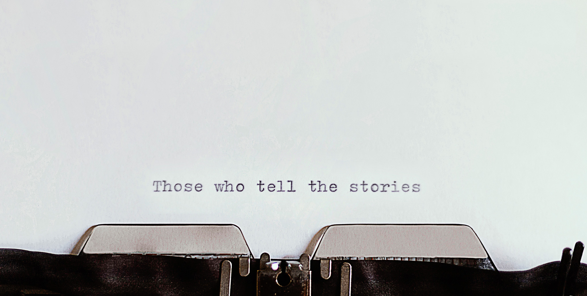 A vintage typewriter with words typed on white paper that say those who tell the stories.